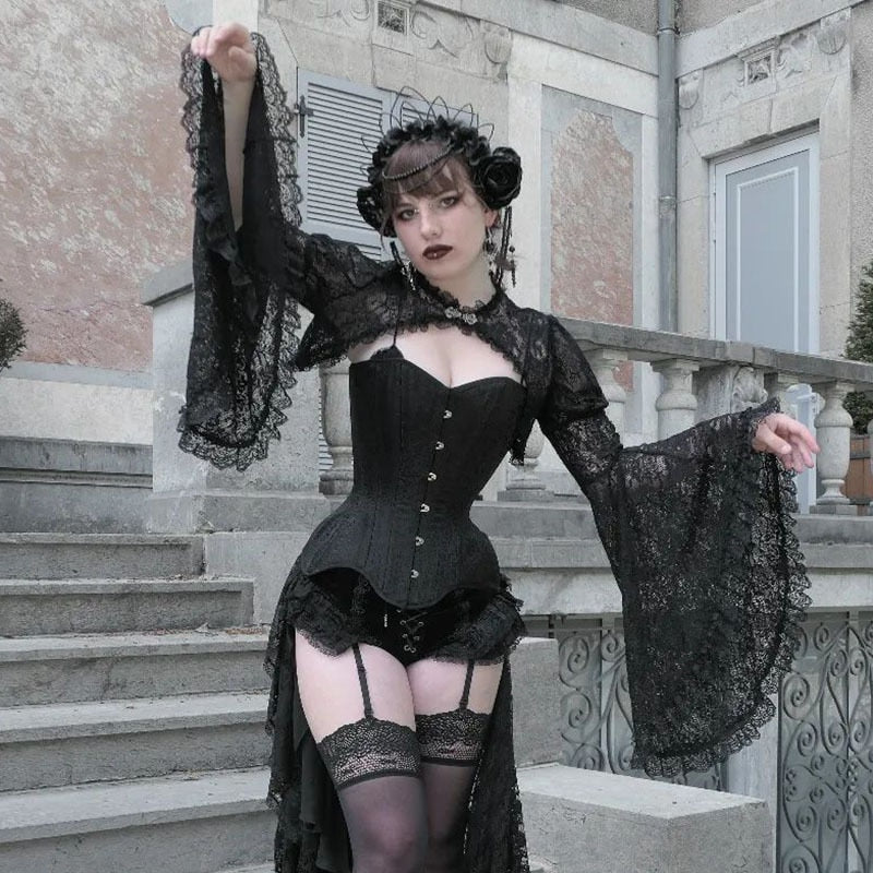 Black floral lace overlay worn over a corset, with one arm lifted beside pale stone stairs and an ornate railing.