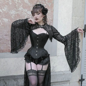 Gothic outfit beside a stone wall, showing the black lace overlay's cropped front, ornate clasp and flared sleeves over a separate corset.