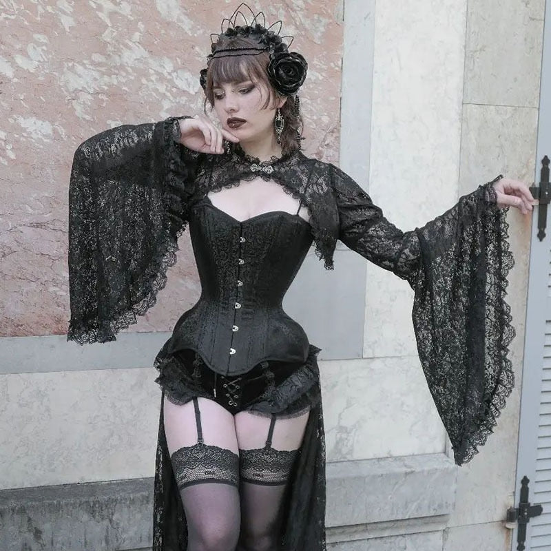 Gothic outfit beside a stone wall, showing the black lace overlay's cropped front, ornate clasp and flared sleeves over a separate corset.