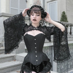 Model holding both hands beside a black headpiece, spreading the ruffled bell sleeves of a black lace overlay over a corset.