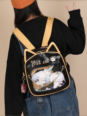 Rear outfit view of the cat-ear backpack with golden-orange shoulder straps, black bat wings and small white plushies displayed in the front window.