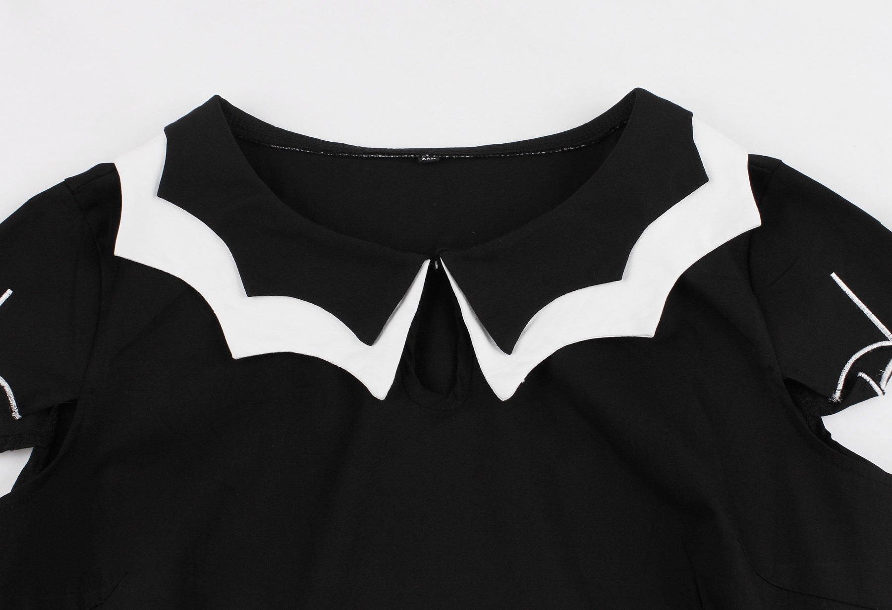 Close view of the white bat-wing collar and front keyhole opening on the black dress.