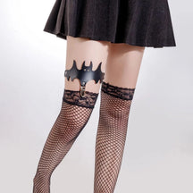 Black bat-shaped leg garter worn above lace-top stockings, with outstretched wings and a central stocking clip.