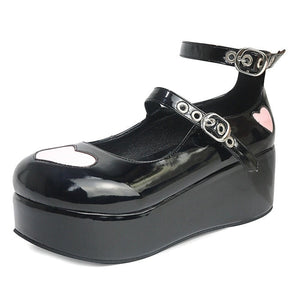 Glossy black platform Mary Jane with pink heart appliques and two grommeted buckle straps, showing the reflective finish from the side.