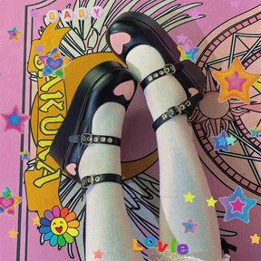 Black big-heart platform Mary Janes worn with pale green socks over a colorful illustrated backdrop, showing the pink toe hearts and grommeted straps.