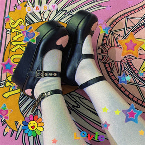 Angled top view of black platform Mary Janes with pink heart toes and double buckle straps, worn with pale green socks over a colorful print.