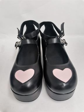 Pair of matte black big-heart platform Mary Janes photographed from above, with large pink toe hearts and crossed buckle straps.
