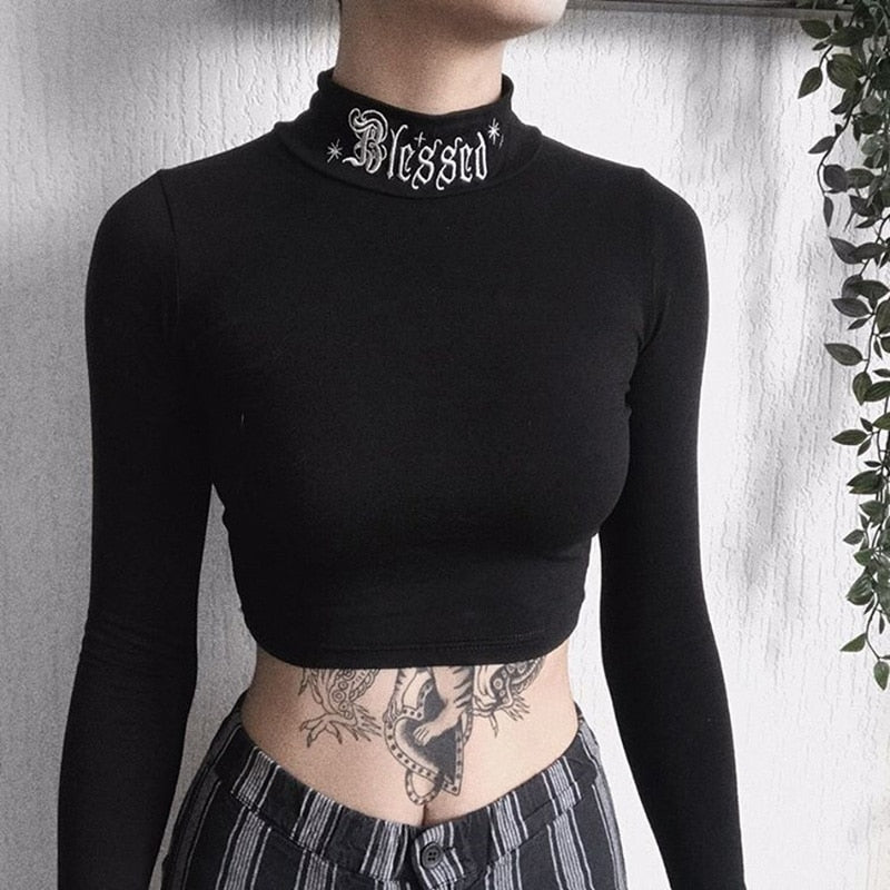 Black Blessed embroidered turtleneck crop top shown from the front with the cropped hem visible.