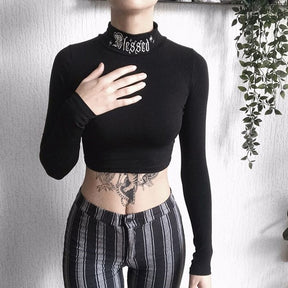 Black Blessed embroidered turtleneck crop top shown in a front outfit with striped trousers.