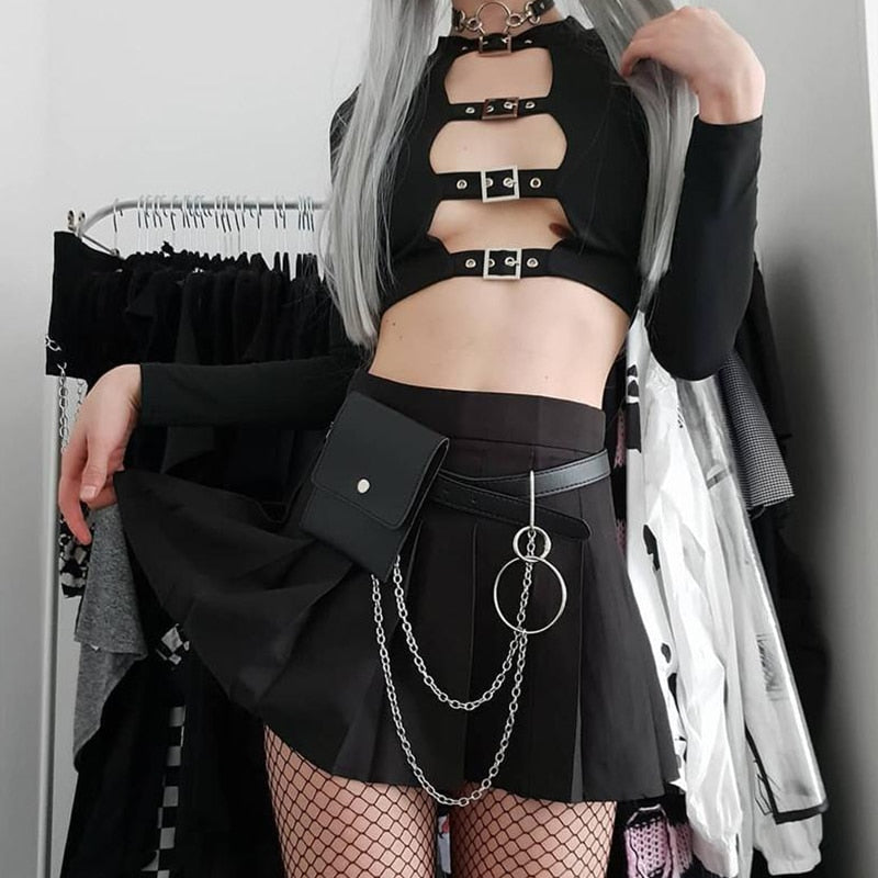 Black cutout buckle crop top styled with a short chain-trimmed skirt and fishnet tights, showing the cropped hem and long sleeves.