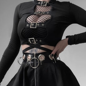Black long sleeve buckle crop top layered over fishnet, with four silver-tone buckles framing the open front above a belted black skirt.