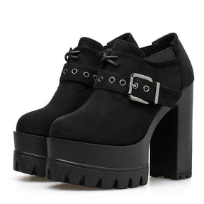 Pair of black faux-suede ankle booties with rounded toes, short lace-up fronts and wide eyelet buckle straps above tall platforms and block heels.