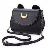 Black cat-ear shoulder bag on white, with a gold-tone crescent on the curved flap and its adjustable chain-detail strap arranged in front.