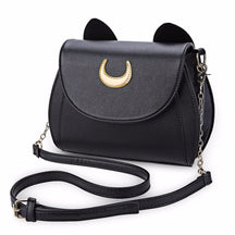 Black cat-ear shoulder bag on white, with a gold-tone crescent on the curved flap and its adjustable chain-detail strap arranged in front.