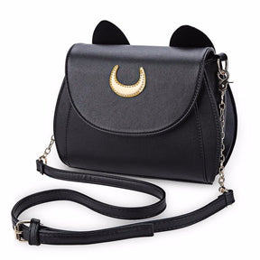 Black cat-ear shoulder bag on white, with a gold-tone crescent on the curved flap and its adjustable chain-detail strap arranged in front.