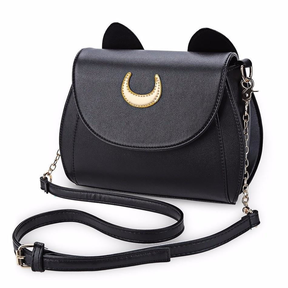 Black cat-ear shoulder bag on white, with a gold-tone crescent on the curved flap and its adjustable chain-detail strap arranged in front.