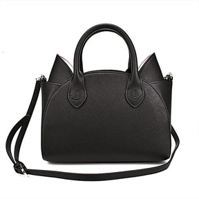 Rear view of the black cat-ear handbag with a plain textured back panel, twin handles and the long shoulder strap looped across the bag.
