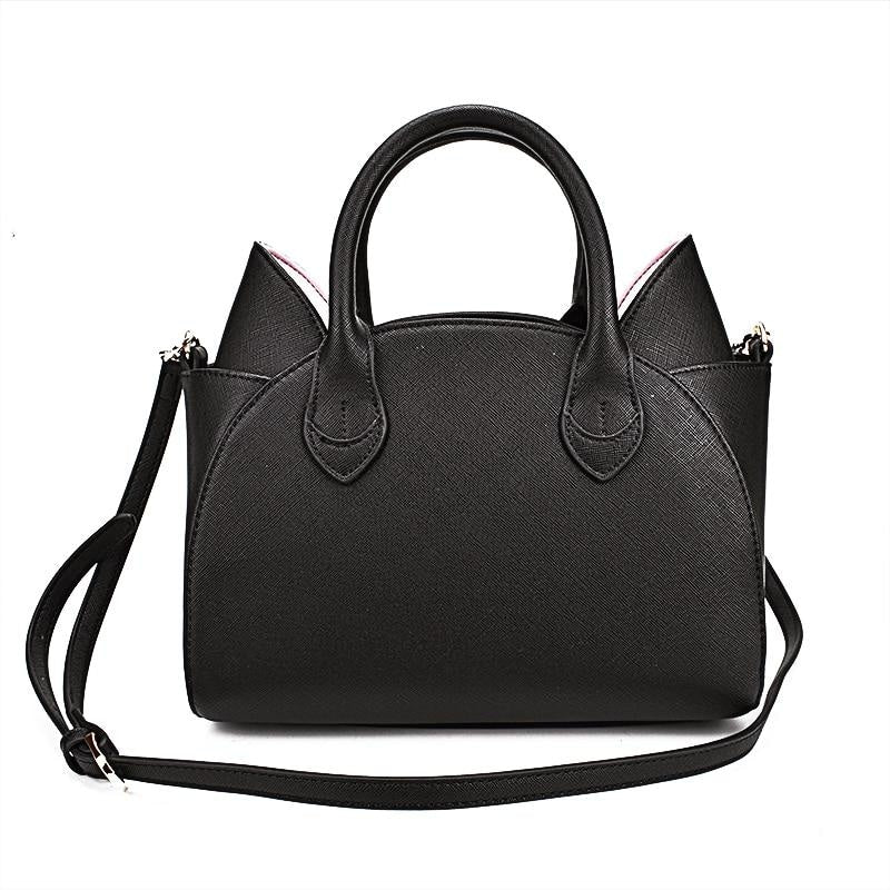 Rear view of the black cat-ear handbag with a plain textured back panel, twin handles and the long shoulder strap looped across the bag.