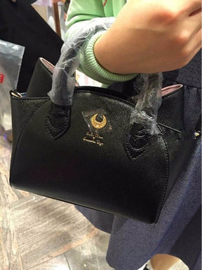 The black cat-ear handbag is carried by its wrapped handles over an arm, showing the crescent emblem and rounded body at close range.