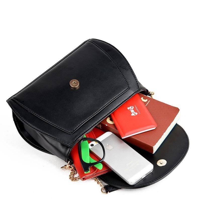 Black cat-ear bag with its flap open and magnetic snap visible. A phone, wallet and small objects are arranged inside to illustrate the interior.