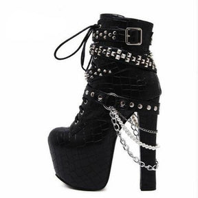 Side view of a black platform ankle boot on white, with silver-tone studded straps, hanging chains, pearl-like beads and a tall rectangular heel.