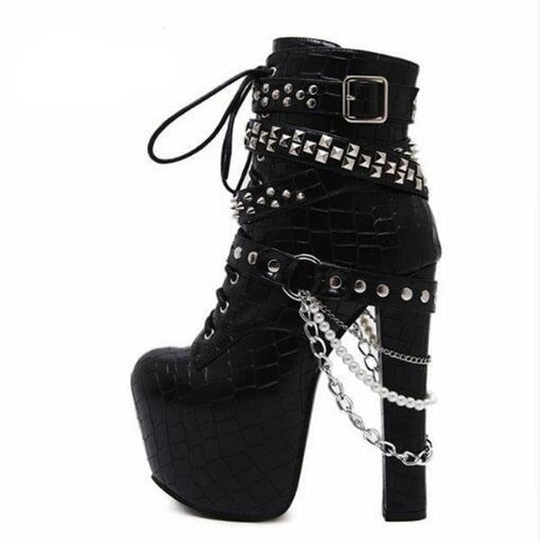 Side view of a black platform ankle boot on white, with silver-tone studded straps, hanging chains, pearl-like beads and a tall rectangular heel.