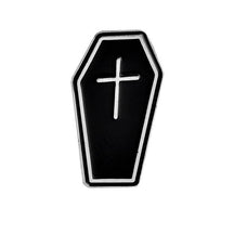 Black coffin-shaped enamel pin with a silver-tone border and a small cross on its front.