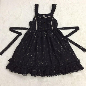 Black star-print pinafore dress laid flat with its long waist ties extended to either side.