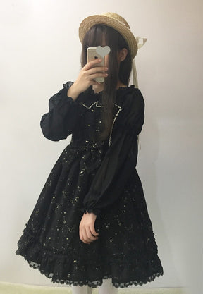Black constellation dress layered over a separate long-sleeve blouse in a mirror outfit photo, styled with a straw hat.