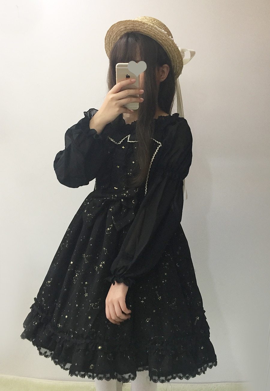 Black constellation dress layered over a separate long-sleeve blouse in a mirror outfit photo, styled with a straw hat.