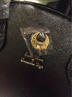 Close-up of the gold-tone crescent and small gold script on the textured black handbag, with protective film visible on the crescent.