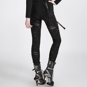Black destroyed skinny pants in an angled front view, with ragged openings down both legs and a narrow hem, styled with buckled high-heeled boots.