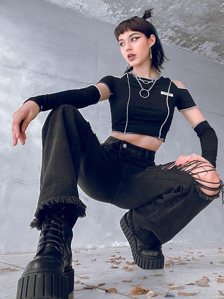 A model crouches in black ripped flare jeans and chunky lace-up boots, showing the distressed knee openings and wide frayed hems.