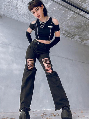 Full outfit view of black distressed flare jeans with an asymmetric high waistband, styled with a cutout crop top and platform boots in a concrete interior.