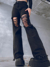 Low-angle view of black high-waisted flare jeans with wide laddered rips over the thighs and knees, frayed hems and chunky platform boots against a concrete wall.