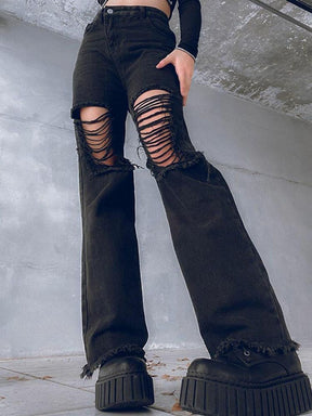 Low-angle view of black high-waisted flare jeans with wide laddered rips over the thighs and knees, frayed hems and chunky platform boots against a concrete wall.