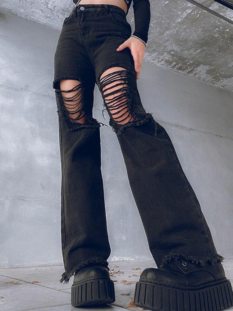 Low-angle view of black high-waisted flare jeans with wide laddered rips over the thighs and knees, frayed hems and chunky platform boots against a concrete wall.