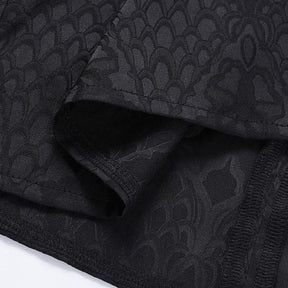 Close-up of folded black cheongsam fabric, showing the tonal dragon-scale motif and stitched hem edge.