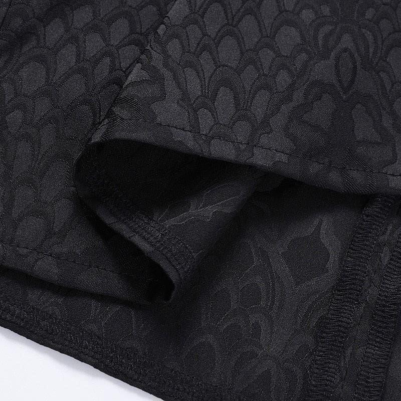 Close-up of folded black cheongsam fabric, showing the tonal dragon-scale motif and stitched hem edge.