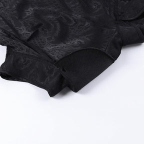 Detail of the cheongsam's short sleeve and finished edge, with black tonal dragon and scale motifs visible across the fabric.