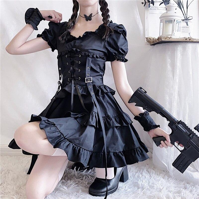 Seated black gothic dress outfit with the layered skirt spread over one knee and a costume prop beside the wearer.