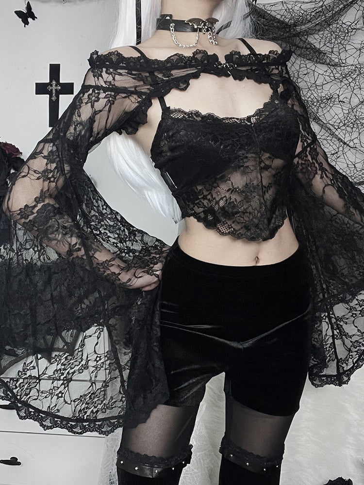 Black gothic lace shoulder overlay worn over a lace camisole and velvet shorts, with one wide bell sleeve spread outward. A white wig and dark wall decorations frame the outfit.