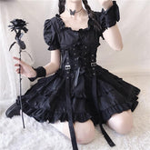 Black gothic puff-sleeve dress worn with a lace-up corset harness and layered ruffle skirt, pictured with a black rose.