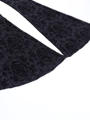 Both flared hems of the black gothic pants spread across a pale surface, revealing the width of the legs and repeating ornate pattern.