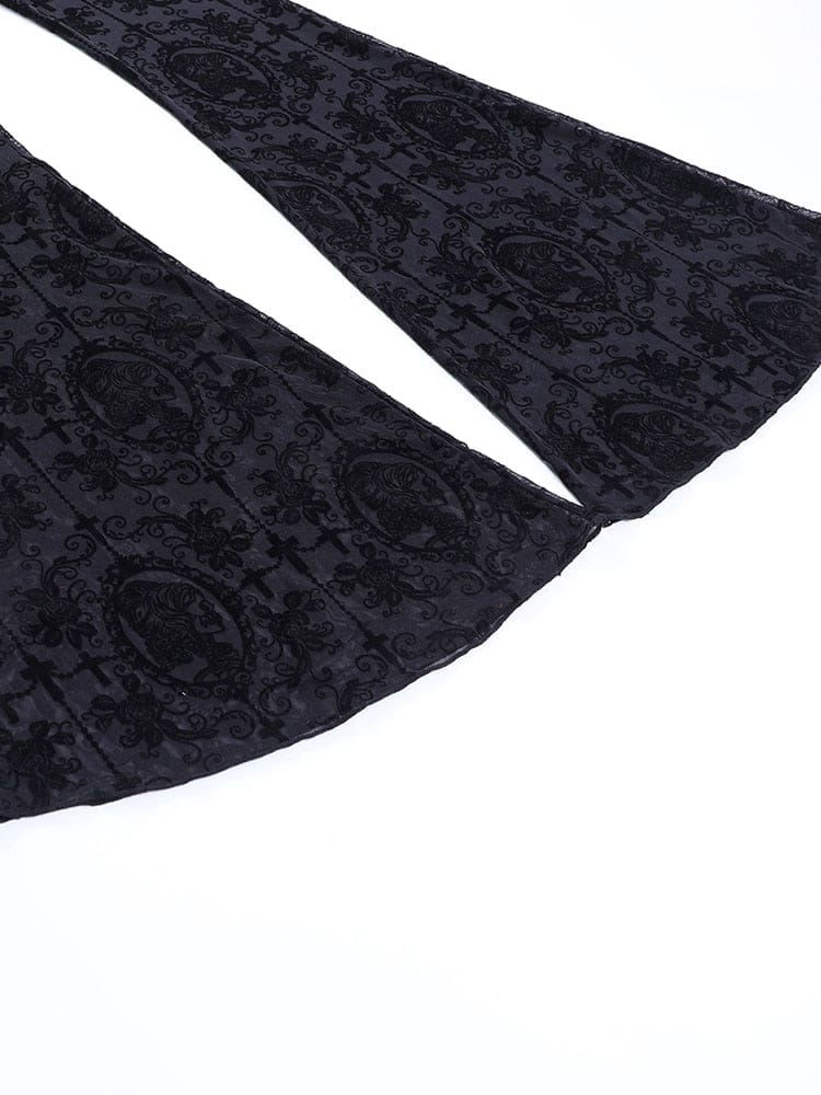 Both flared hems of the black gothic pants spread across a pale surface, revealing the width of the legs and repeating ornate pattern.
