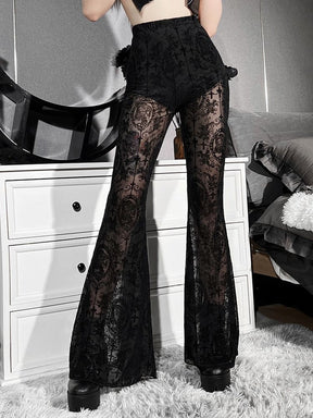 Angled hip view of black sheer bell bottom pants with one hand resting at the waist. The dense pattern contrasts with the translucent mesh.