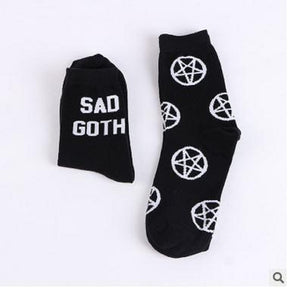 Two black sock designs displayed together on white: a folded Sad Goth sock on the left and a longer sock covered in white pentagrams on the right.