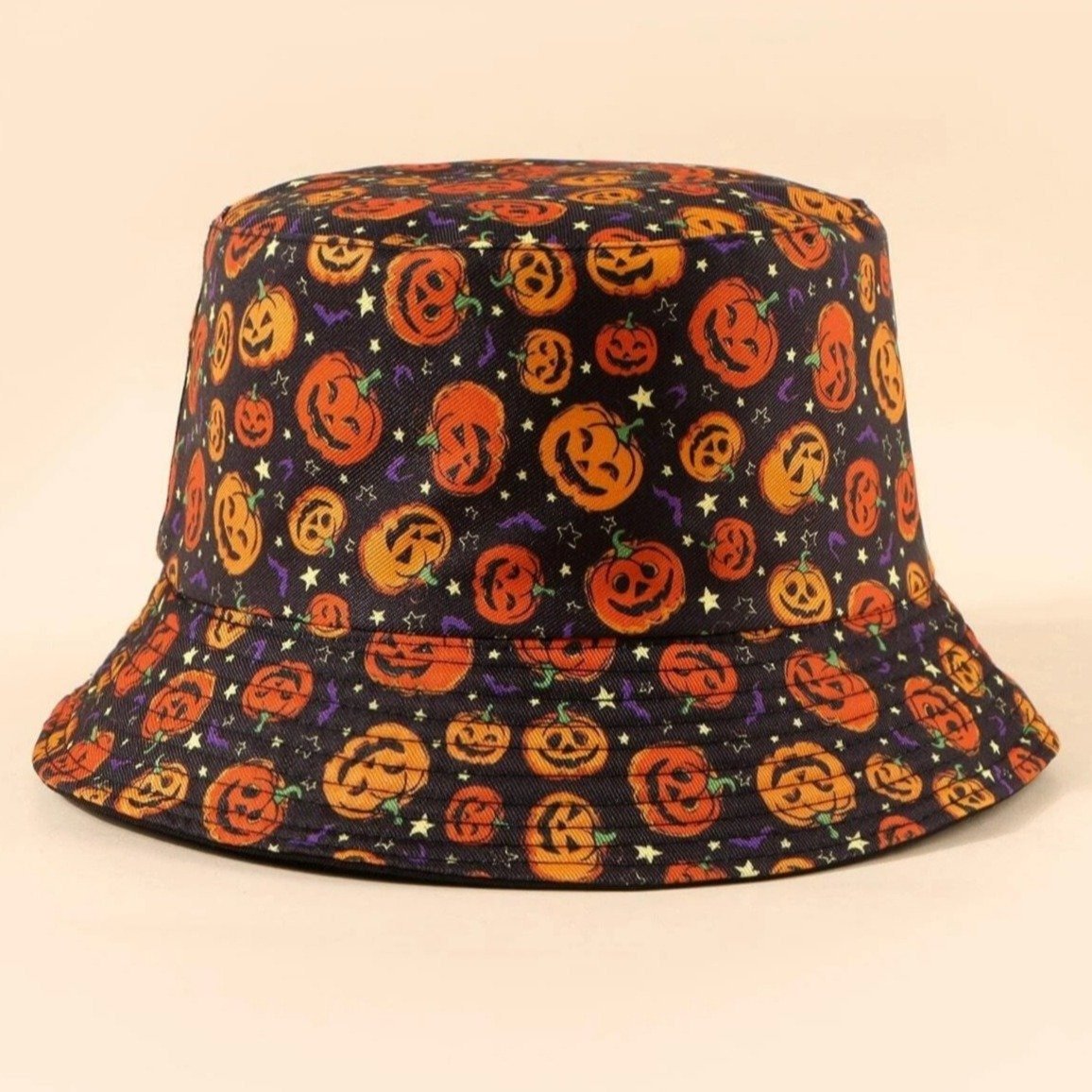 Black bucket hat with orange pumpkin faces photographed against a warm pale background. Rows of stitching follow the curved brim.