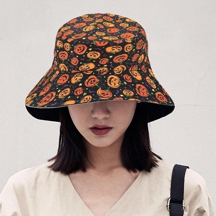 Model wearing the black pumpkin-print bucket hat with a light V-neck top. The orange patterned brim curves down over the forehead.