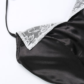 Detail of one white lace lapel against the glossy black bodice beside a thin halter strap.